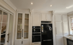 Mobilier bucătărie din lemn masiv în stil clasic alb, cu detalii sculptate, vitrine sticlă și încadrare electrocasnice