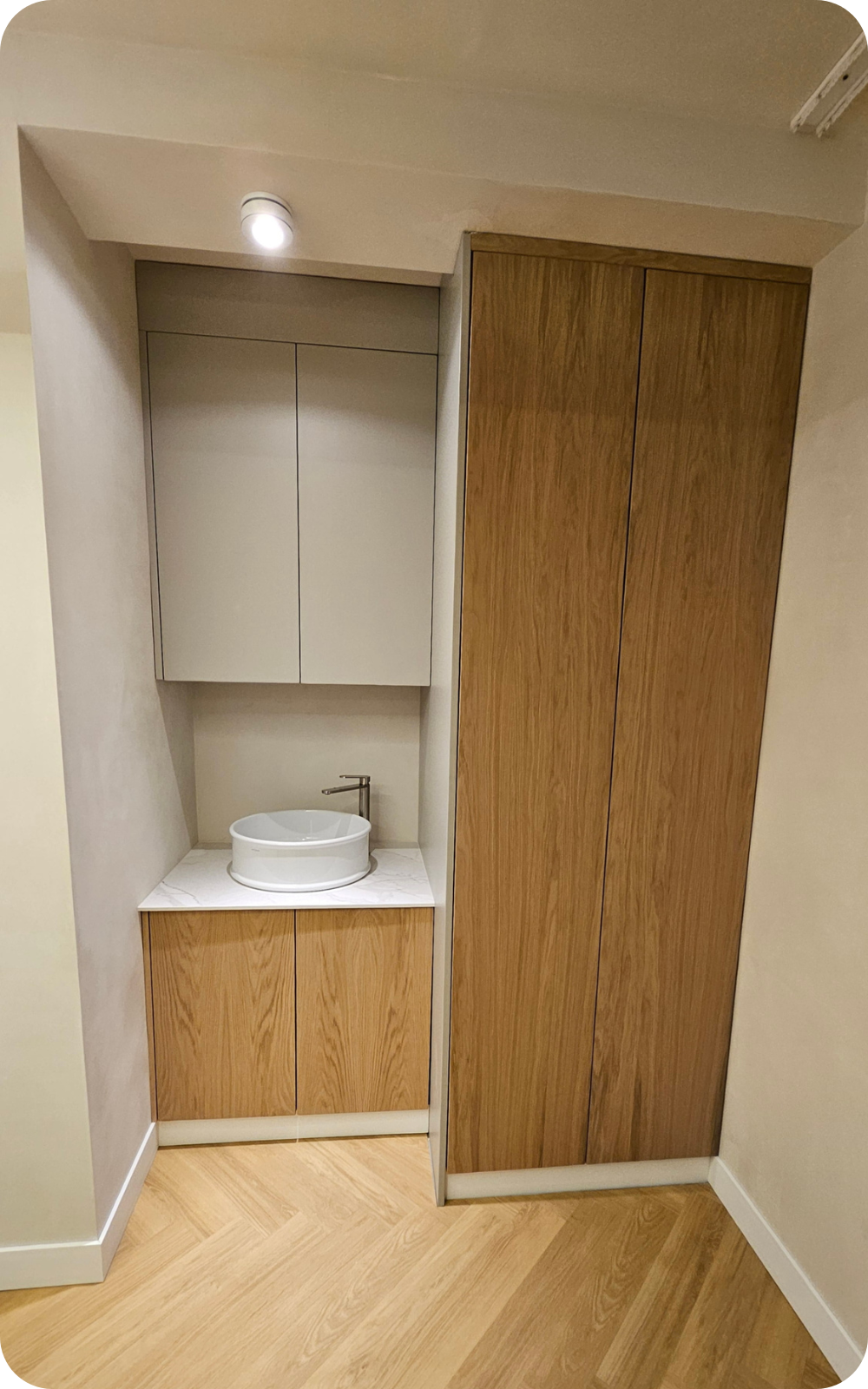 Mobilier încastrat de baie cu blat alb, lavoar ceramic rotund și dulap din lemn natur