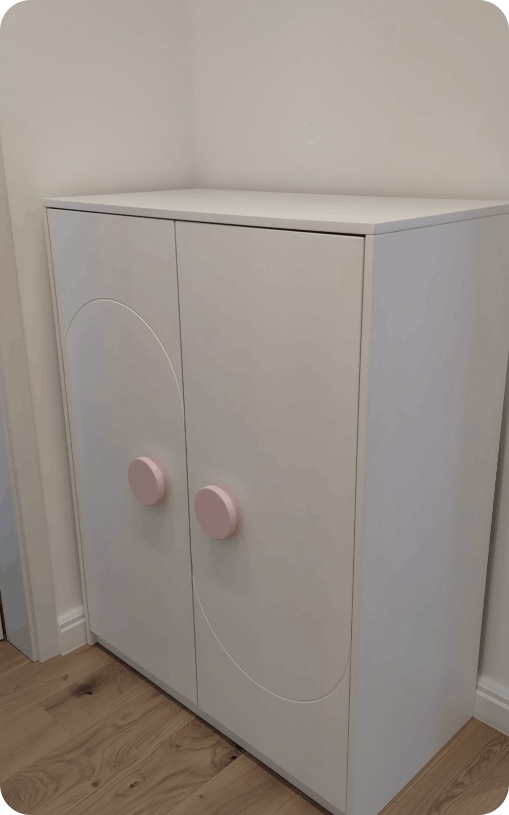 Comodă albă joasă pentru camera copiilor cu frezaje decorative și mânere roz pastel pentru uși din lemn masiv