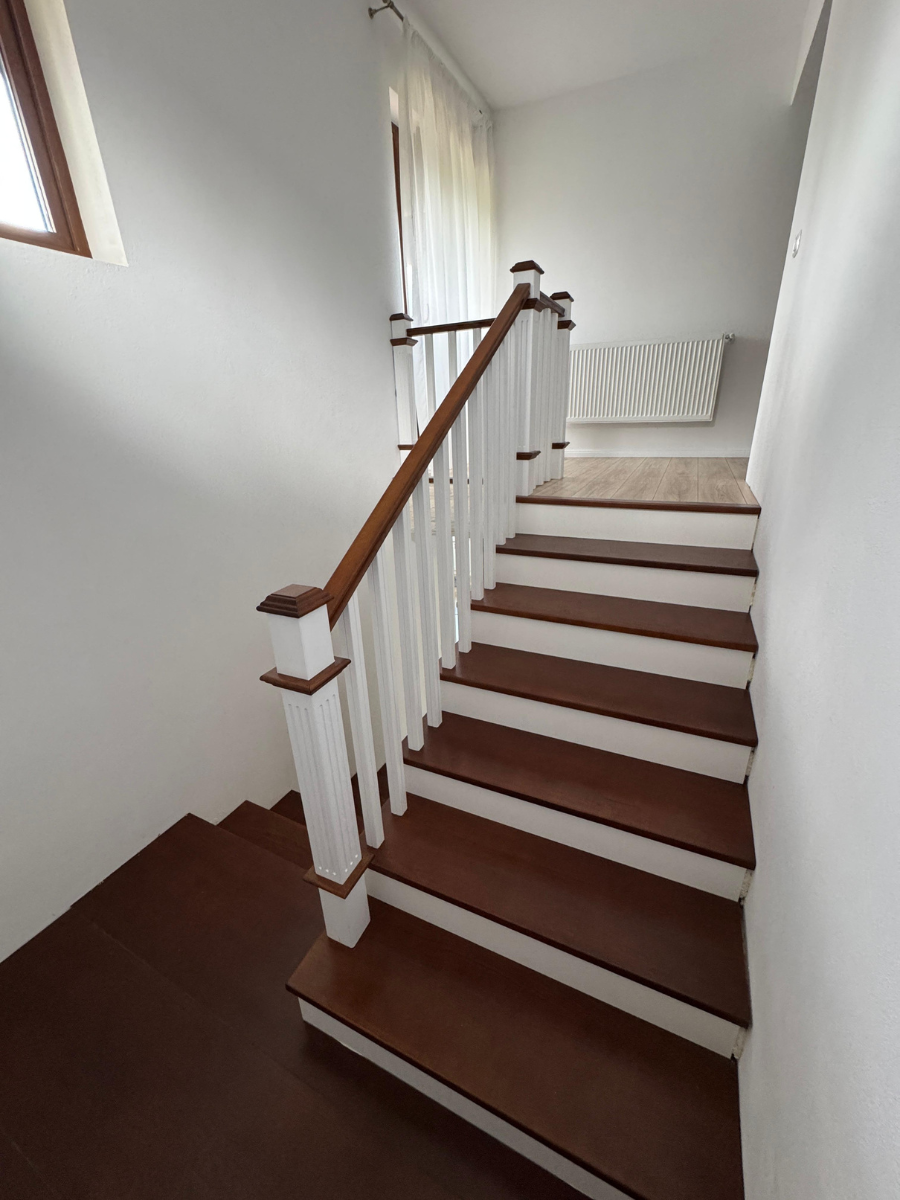 Scară interioară din lemn în nuanță închisă cu balustradă albă, baluștri verticali și mână curentă din lemn