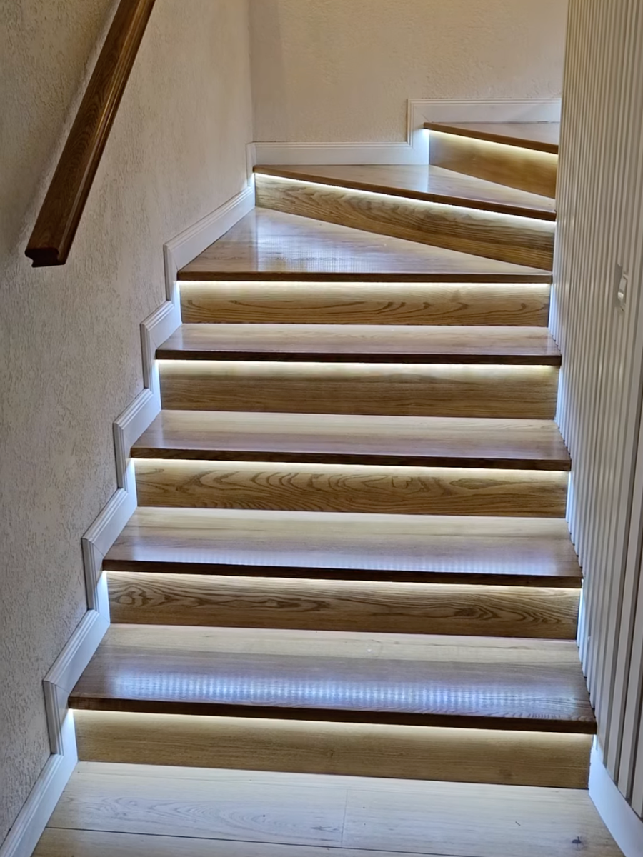 Scară interioară modernă din lemn masiv cu trepte iluminate LED și plintă albă decorativă