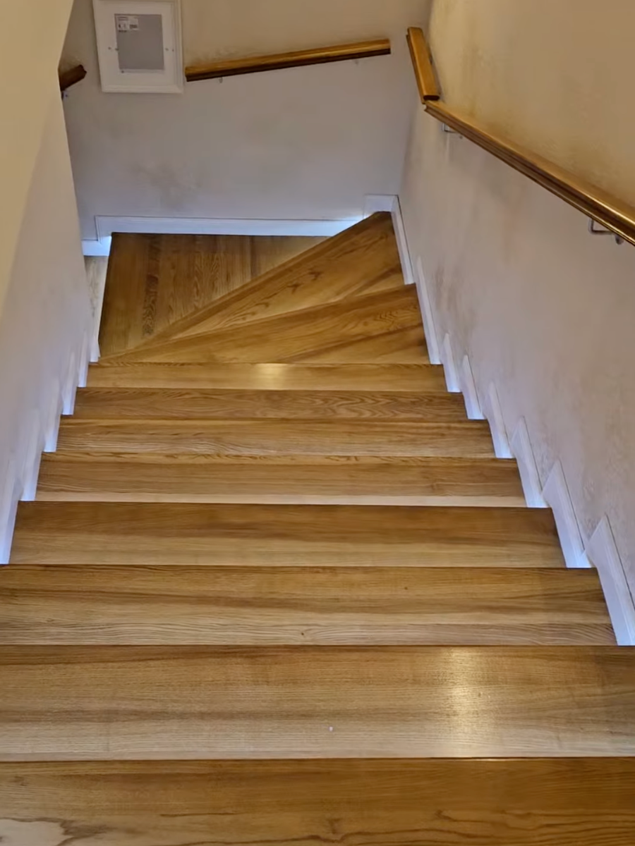 Vedere de sus a unei scări balansate din lemn masiv cu mână curentă montată pe perete și finisaj satinat